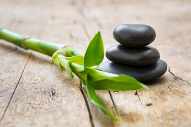 Close up of stacked hot stones with green bamboo on wooden table. Black massage stones necessary for a hot rock treatment in a spa setting. Beauty and spa treatment concept.
